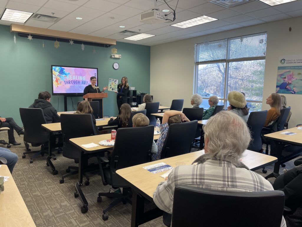 A client of Mind & Spirit Counseling Center shares the inspiration behind their art piece at the gallery event.